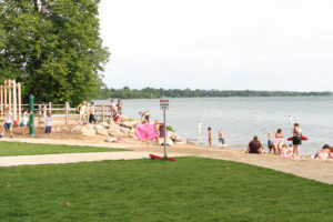 A beach on a lake in a park with people relaxing on the sand and in the water